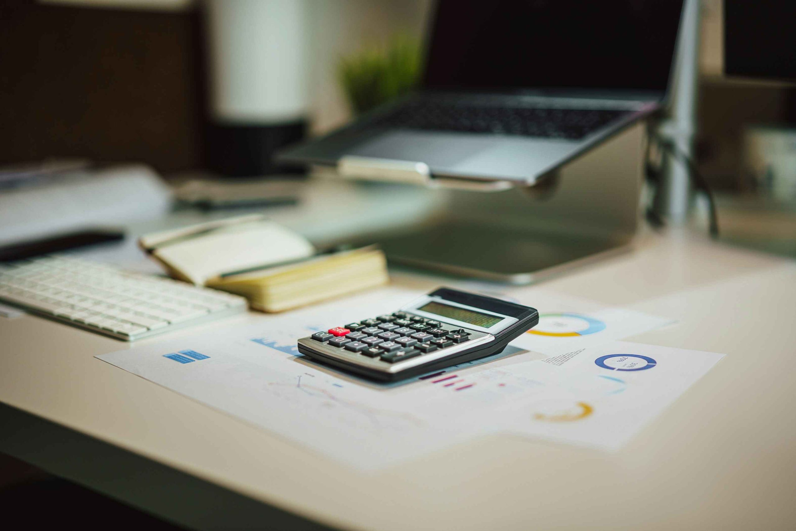 A calculator sits on financial documents next to a keyboard, notebook, and an open laptop on a desk in an office setting—capturing the organized workspace of a fee-only fiduciary financial advisor in Reno.