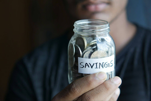 A person holds a glass jar labeled “SAVINGS” filled with coins, symbolizing efforts to reduce your RMDs and build a more secure financial future.